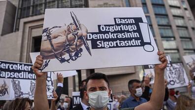 People wearing COVID masks are putting up posters which say "Freedom of the press is the insurance of democracy!" and "The truth cannot be imprisoned!" in Turkish in front of a court building in Istanbul