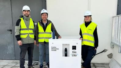 Three people in hard hats and high-vis vests stand beside an Eau de L'Air water dispenser.
