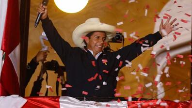 Pedro Castillo saluting the people wearing a sombrero, with a Peruvian flag on the back
