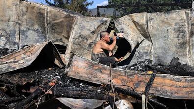 A man drinking water while sitting on the ashes of his mobile home, which burned down during a fire in California