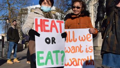 Two people carrying banners that say "Heat or eat?" and "All we want is warmth"