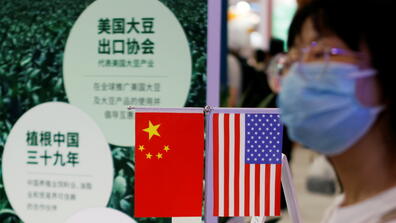 A woman walks past Chinese and US flags displayed at the US Soybean Export Council booth during the 2021 China International Fair for Trade in Services (CIFTIS) in Beijing
