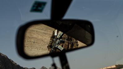 A member of Afghan armed forces is reflected in the rearview mirror of a car