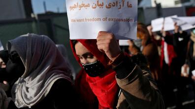 Afghan women protest in Kabul, one carrying a banner that says "We want freedom of expression."
