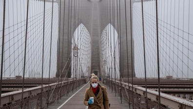 A woman holding a cup of coffee at the Brooklyn Bridge seen on the background