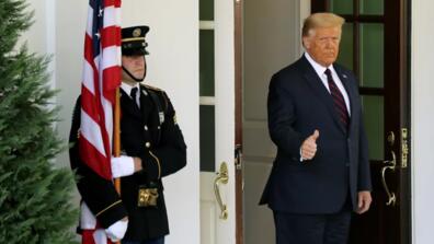 President Trump gives a thumbs up at the side of a soldier holding an American flag.