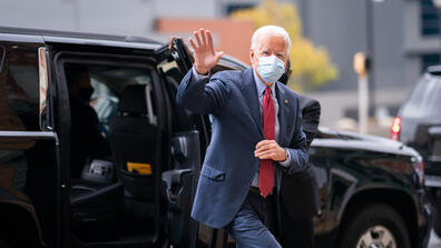 Biden wearing a mask waves as he walks