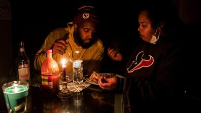 Two people eat at a table lit by only candlelight