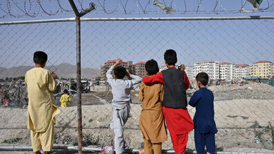 Children watch people at a camp for internally displaced people where new apartment buildings are located in Kabul
