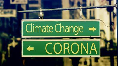 Two road signs pointing in different directions. One says Climate Change and the other says Corona.