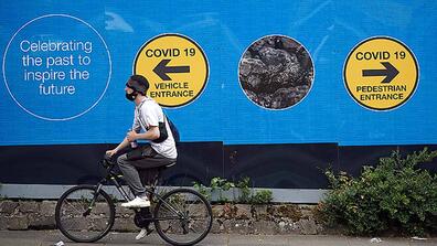 A bicycler following the sign COVID 19 vehicle entrance in front of a wall