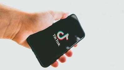 Against a white background, a hand holds a phone with the Tiktok logo on its screen