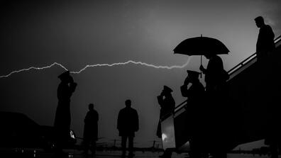 lightning strikes across the sky behind a group of silhouettes with umbrellas