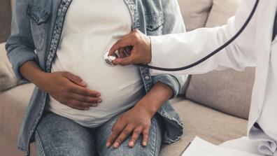 A doctor uses a stethoscope listens to the belly of a pregnant Black woman