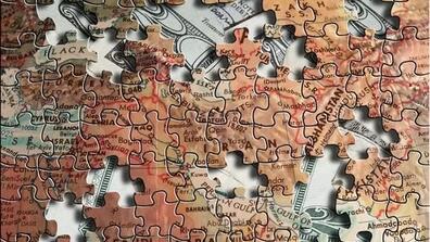 A puzzle made out of a map of the Middle East, with pieces missing to reveal U.S. dollars behind it.