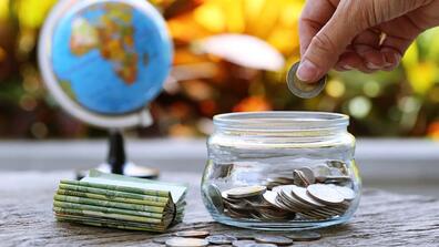 A hand places a coin in a glass jar of coins