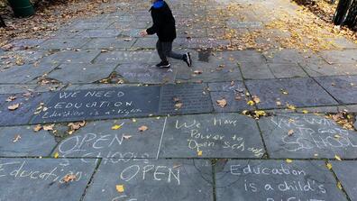 Child runs across a sidewalk in front of New York's City Hall decorated with graffiti in favor of keeping open public schools. 