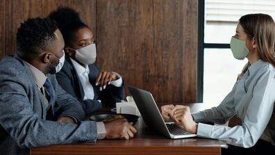 Three people working at a table, each wearing a face mask