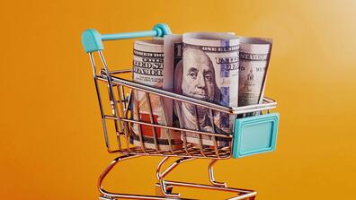 Miniature shopping cart filled with rolled up hundred dollar bills