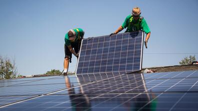 two workers install solar panels onto the roof of a house