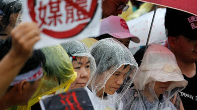 Protesters gather in the rain during a rally against pro-China media in front of the presidential office building in Taipei on June 23, 2019