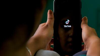 Hands holding a phone with the Tiktok logo on the screen