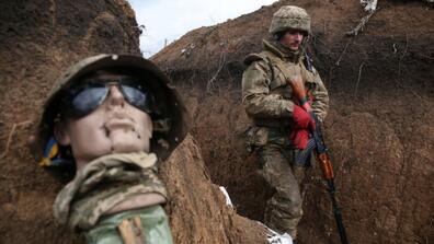 An Ukrainian serviceman walks in a trench by a sort of mannequin as he stands at his post on the frontline 