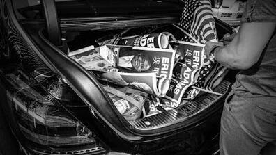Black & white image of a car trunk full of Eric Adams posters in Chinese and a couple of American flags