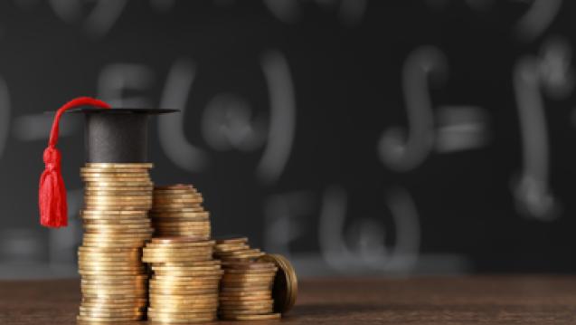 golden coin stacks, tallest stack has graduation cap with red tassel. Background has blurred chalkboard with math equations. 