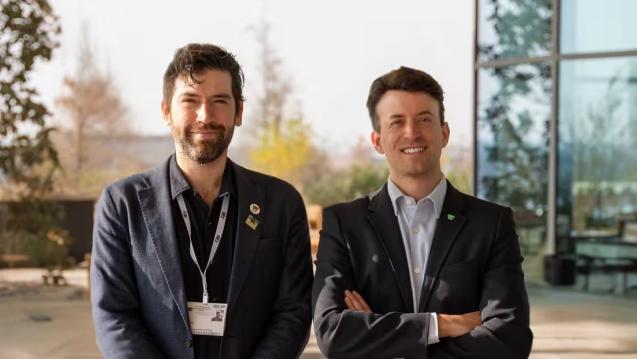 Alfred DeGemmis and Arnaud Goessens standing side by side at a conference, smiling for the camera.