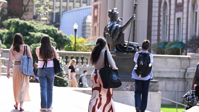 Students carrying bags walk past the Alma Mater statue on Columbia's Morningside campus.