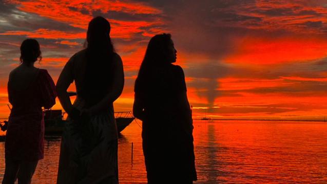 Silhouetted SIPA Capstone students observe a brilliant red-orange sunset over the water.