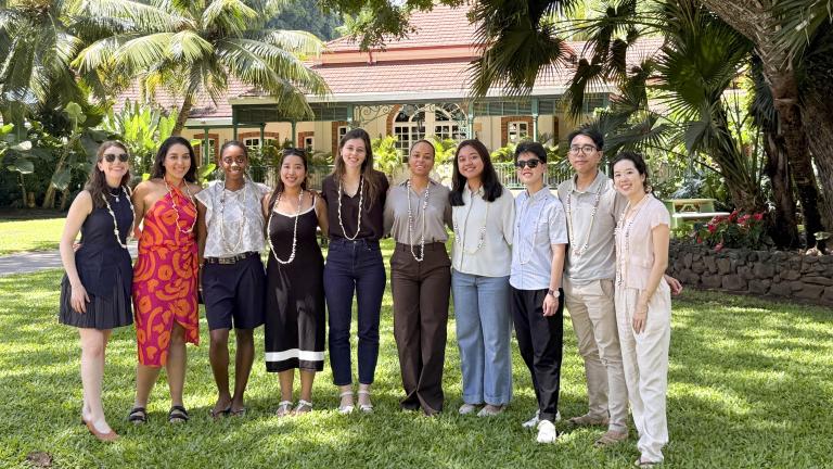 Ten smiling Capstone team members wearing shell leis on a tropical lawn in front of a historic estate.