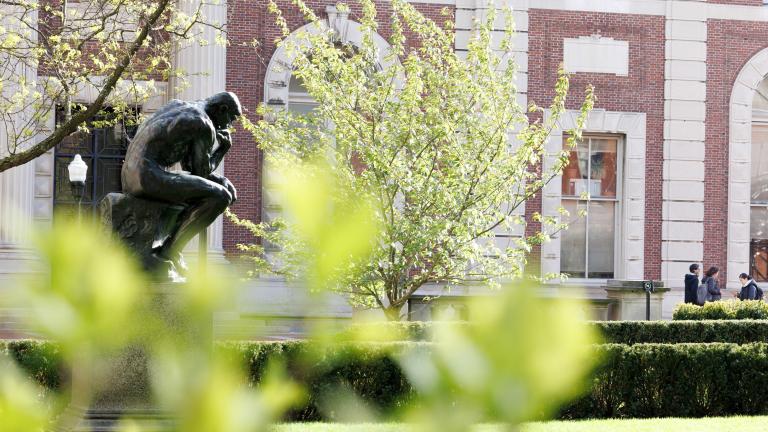 The Thinker statue on Columbia University's campus, framed by bright green foliage.