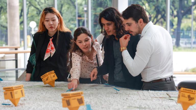 Four SIPA Capstone students gather around a 3D urban planning map, examining location markers.