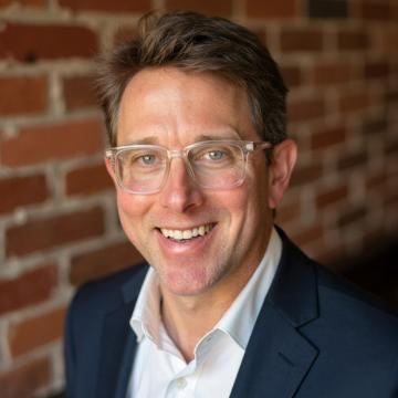 Rick Greenberg, Adjunct Associate Professor, smiling next to a wall.