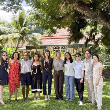 Ten smiling Capstone team members wearing shell leis on a tropical lawn in front of a historic estate.