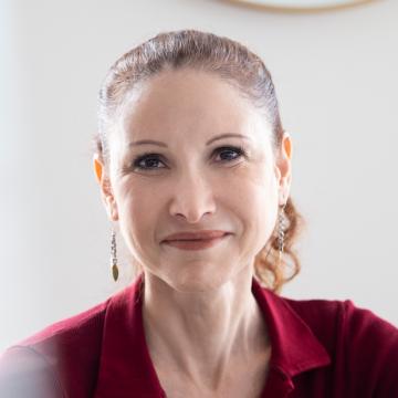 Headshot of Natalia Pasternak Taschner smiling and wearing a red collared shirt and drop earrings.