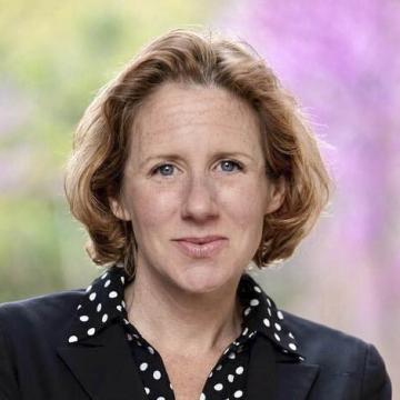 Headshot of Stacie Goddard smiling in a blazer and polka dot shirt against a soft floral background.