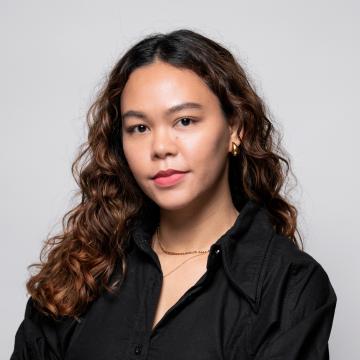 Headshot of Elita waring a black button up in front of a grey backdrop.