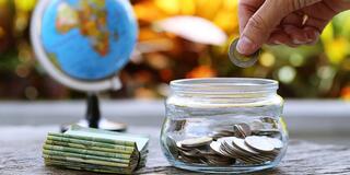 A hand places a coin in a glass jar of coins