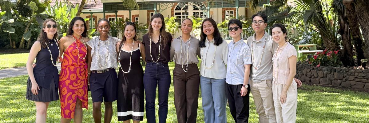 Ten smiling Capstone team members wearing shell leis on a tropical lawn in front of a historic estate.
