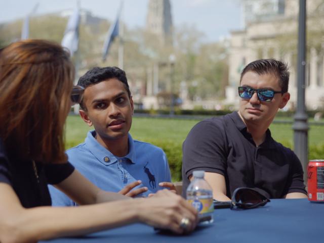 Four college students sitting outdoors around a blue table, engaged in conversation at Columbia University campus.