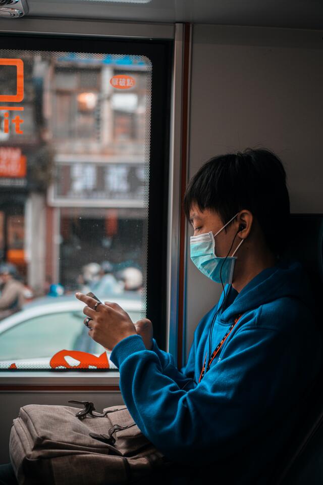 a person wearing a mask uses their phone on a bus