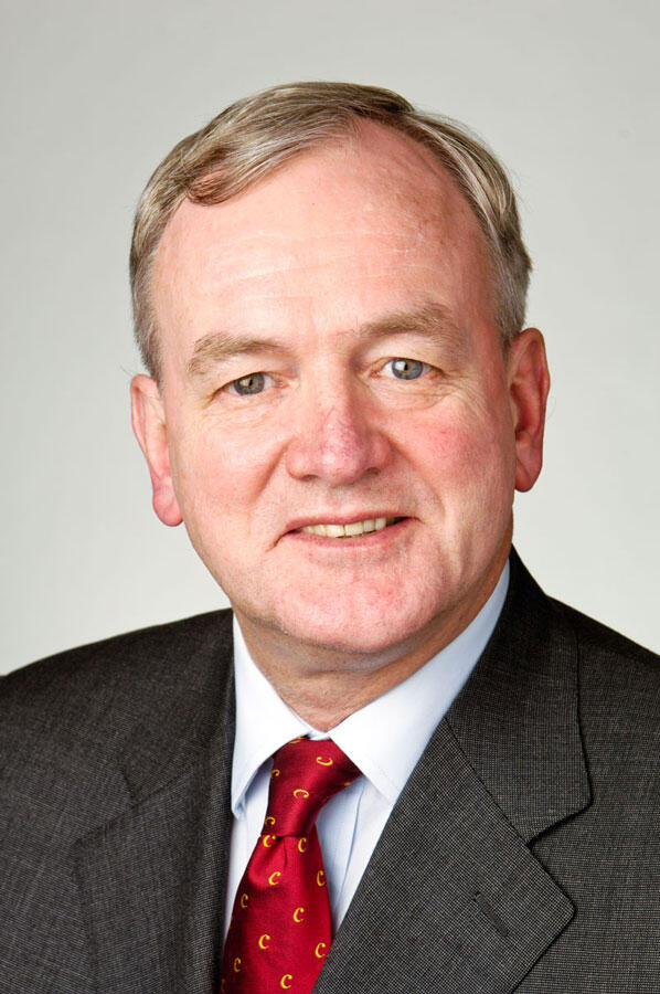 middle-aged caucasian man, blond hair, dark suit, red tie